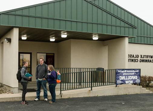 three students stand outside campus building talking to each other